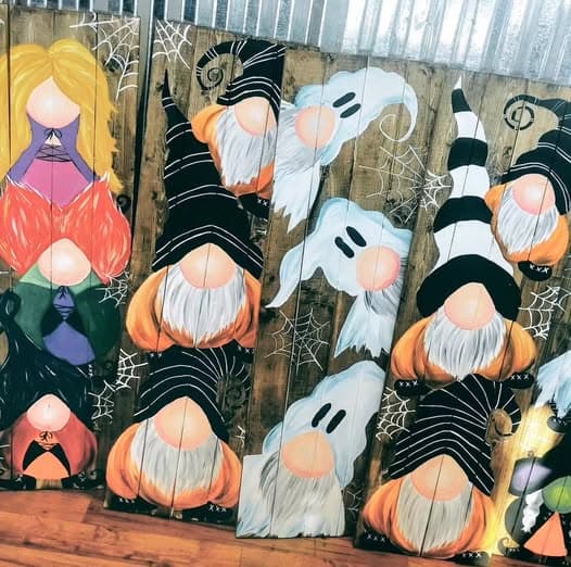 Large painted porch signs on weathered wood slats showing Halloween gnomes in striped outfits with orange pumpkins and ghost accents.