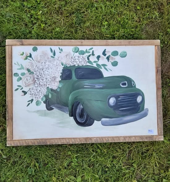 Framed painting of a vintage green pickup truck loaded with white hydrangeas, photographed on green grass.